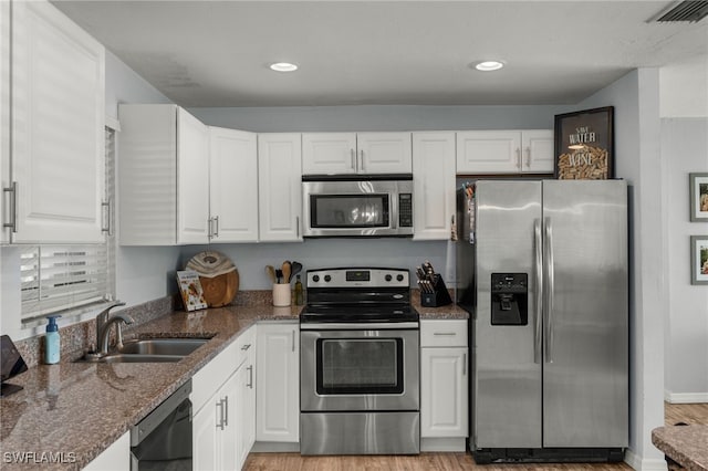 kitchen with white cabinetry, sink, dark stone countertops, stainless steel appliances, and light wood-type flooring