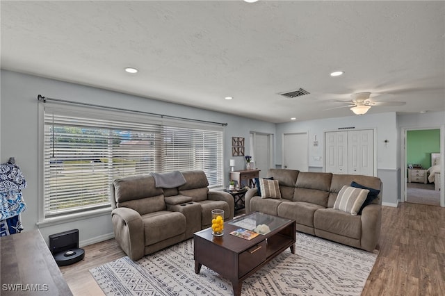 living room with ceiling fan, a textured ceiling, and light wood-type flooring