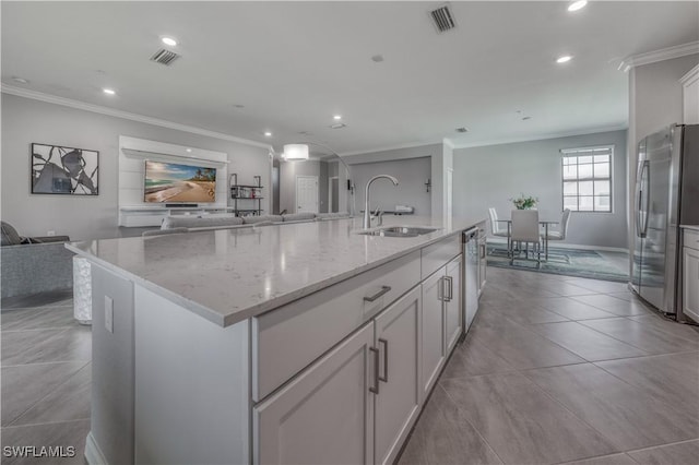 kitchen featuring sink, appliances with stainless steel finishes, white cabinetry, light stone countertops, and a center island with sink