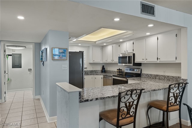 kitchen with a breakfast bar, white cabinetry, appliances with stainless steel finishes, a raised ceiling, and kitchen peninsula