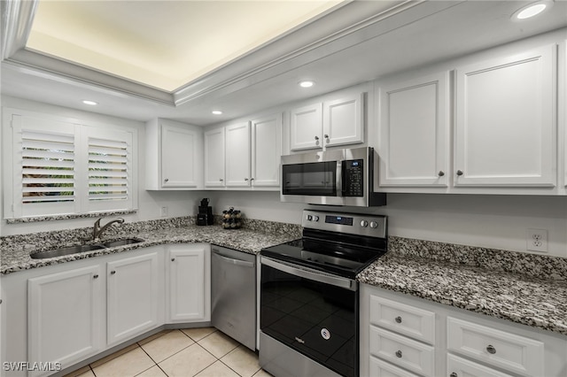 kitchen with sink, light tile patterned floors, appliances with stainless steel finishes, a tray ceiling, and white cabinets