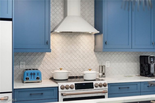 kitchen with high end range, wall chimney range hood, decorative backsplash, and blue cabinetry