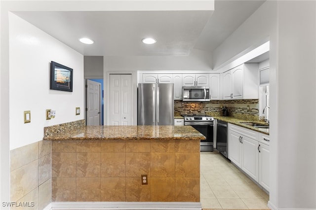 kitchen featuring sink, stainless steel appliances, kitchen peninsula, white cabinets, and dark stone counters