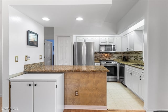 kitchen with stone counters, appliances with stainless steel finishes, white cabinetry, backsplash, and kitchen peninsula