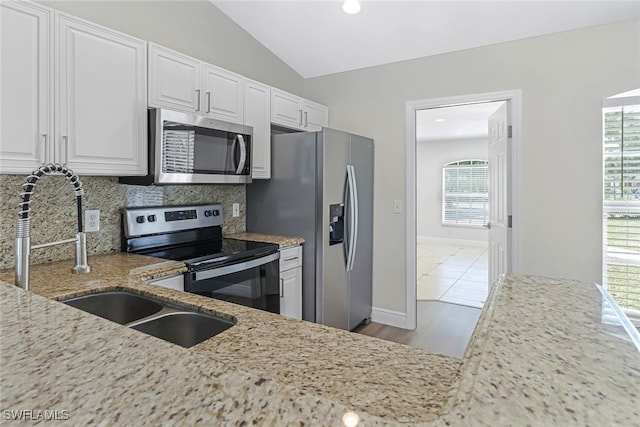 kitchen with lofted ceiling, stainless steel appliances, light stone counters, tasteful backsplash, and white cabinets