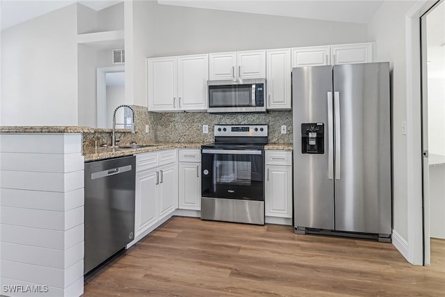 kitchen featuring lofted ceiling, sink, appliances with stainless steel finishes, light stone counters, and white cabinets