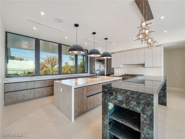 kitchen with hanging light fixtures, light stone counters, white cabinets, and a large island with sink