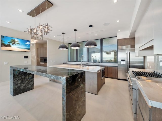 kitchen featuring high quality appliances, light stone countertops, a center island with sink, and decorative light fixtures