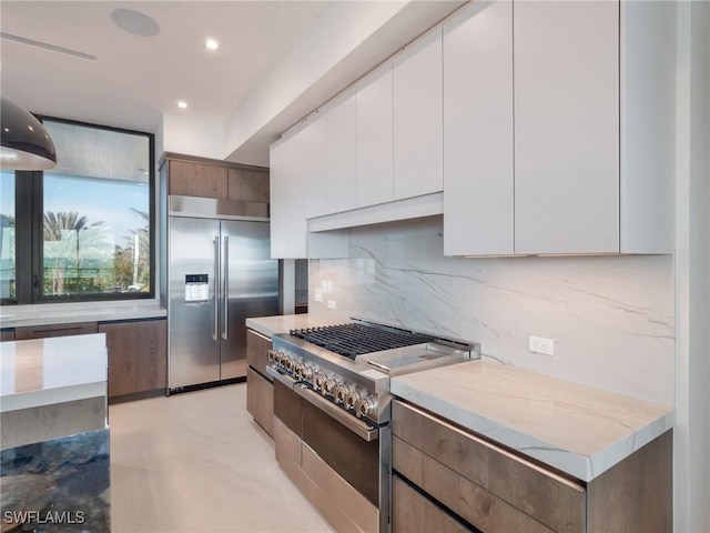 kitchen featuring white cabinetry, high end appliances, backsplash, and light stone counters