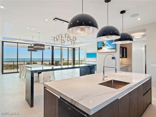 kitchen with sink, black dishwasher, a spacious island, light stone counters, and a water view