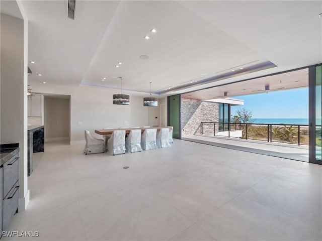 living room featuring a raised ceiling, expansive windows, and a water view