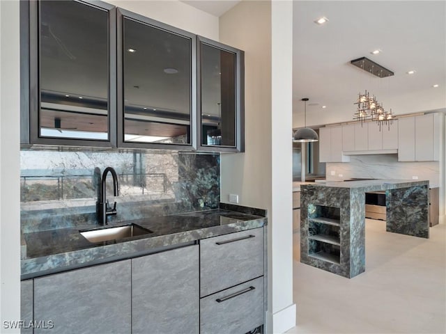 kitchen with hanging light fixtures, sink, backsplash, and dark stone counters