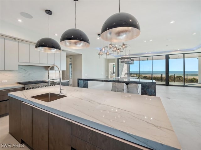 kitchen with dark brown cabinetry, light stone countertops, decorative backsplash, white cabinets, and decorative light fixtures