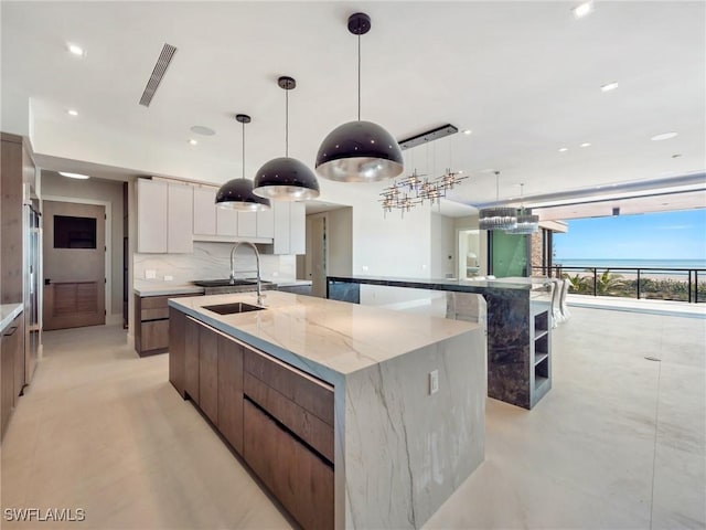 kitchen with hanging light fixtures, a large island with sink, sink, and white cabinets