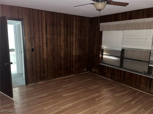 spare room with hardwood / wood-style flooring, ceiling fan, and wood walls