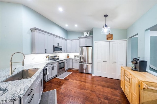 kitchen featuring decorative light fixtures, sink, light stone counters, stainless steel appliances, and dark wood-type flooring