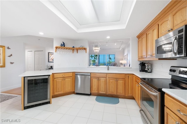 kitchen featuring rail lighting, beverage cooler, light tile patterned floors, kitchen peninsula, and stainless steel appliances