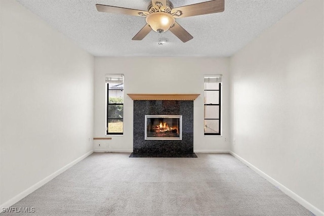 unfurnished living room with ceiling fan, a high end fireplace, light carpet, and a textured ceiling