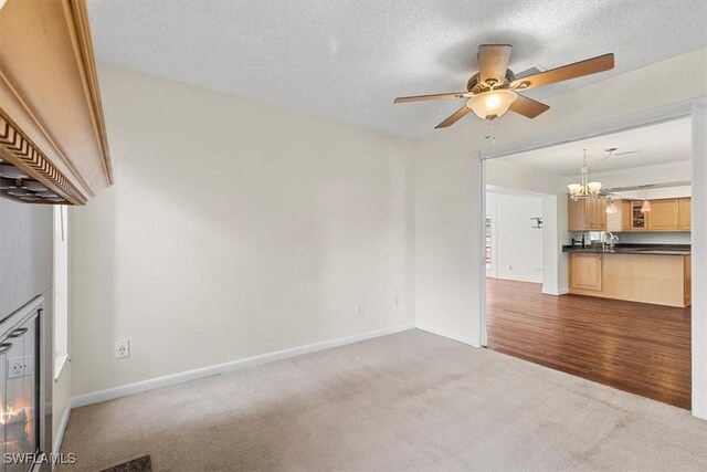 unfurnished living room featuring sink, ceiling fan with notable chandelier, a textured ceiling, and carpet