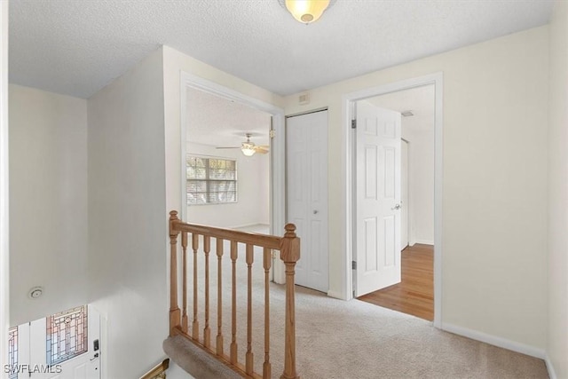 hallway with light carpet and a textured ceiling