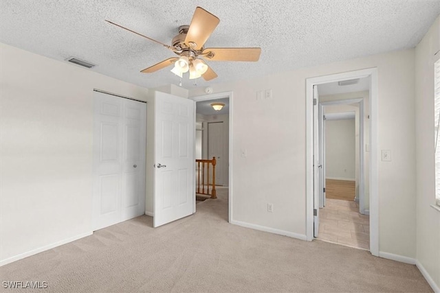 unfurnished bedroom featuring ceiling fan, a closet, light carpet, and a textured ceiling