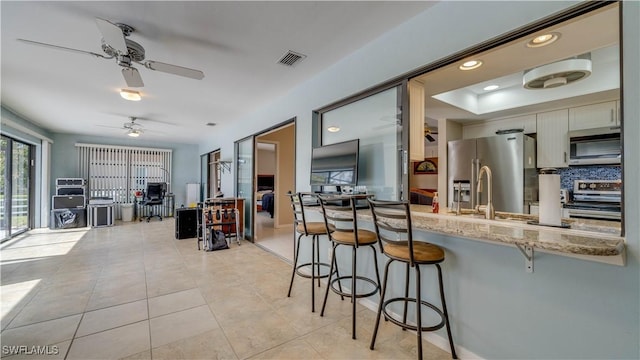 kitchen with tasteful backsplash, a kitchen bar, light tile patterned floors, stainless steel appliances, and light stone countertops