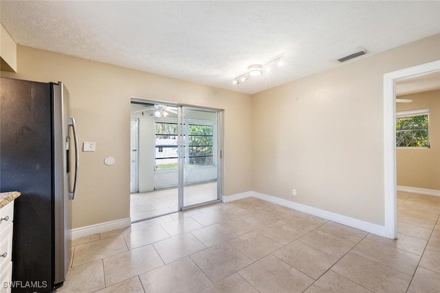 tiled empty room featuring ceiling fan, a textured ceiling, and a healthy amount of sunlight