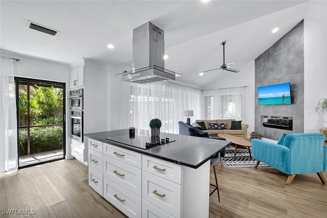 772 Reef Point Cir, Naples, FL 34108 - kitchen with island exhaust hood, black electric stovetop, light wood finished floors, dark countertops, and a ceiling fan
