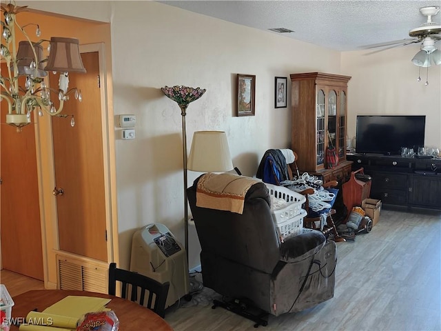 living room with ceiling fan, a textured ceiling, and light wood-type flooring