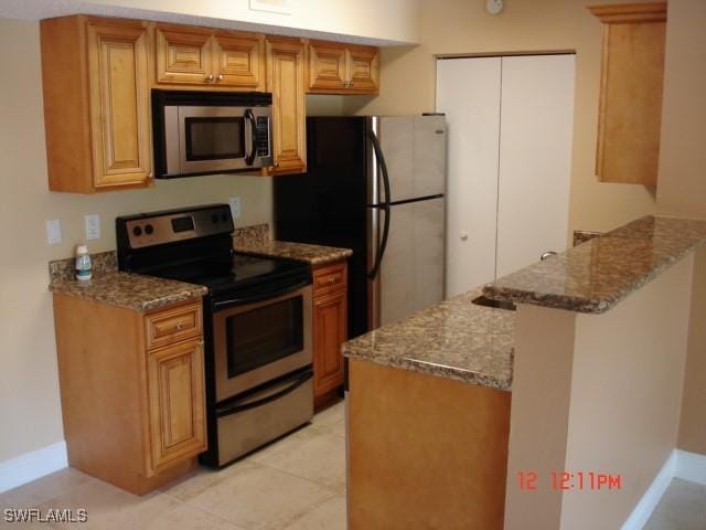 kitchen with appliances with stainless steel finishes, dark stone countertops, light tile patterned floors, and kitchen peninsula