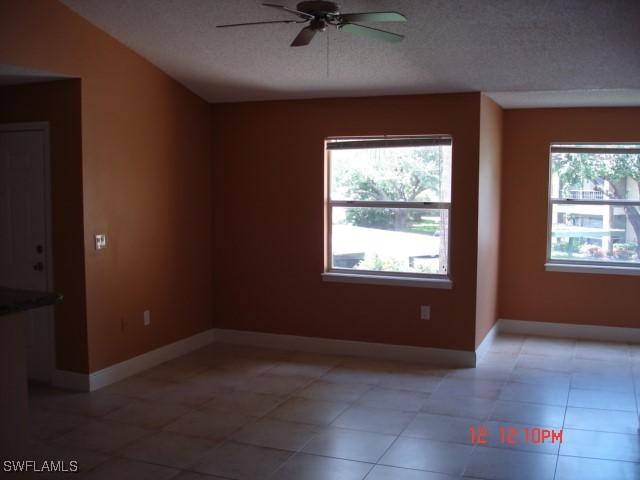 tiled empty room with ceiling fan, a wealth of natural light, and a textured ceiling