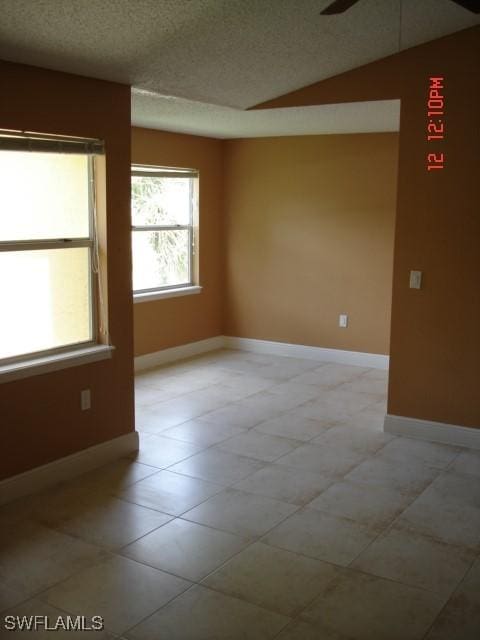 empty room with ceiling fan, vaulted ceiling, and a textured ceiling