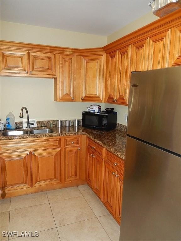 12571 Equestrian Cir Unit 902, Fort Myers, FL 33907 - kitchen with freestanding refrigerator, black microwave, brown cabinetry, light tile patterned floors, and dark stone counters