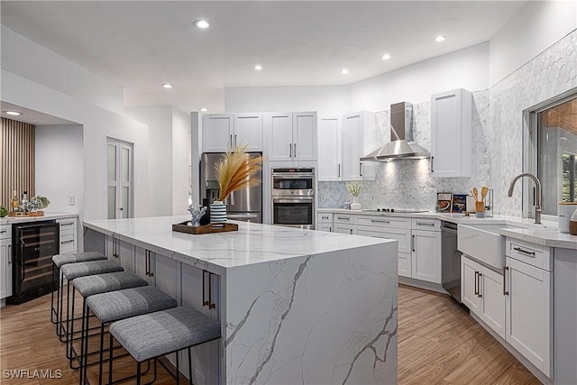 kitchen featuring wine cooler, wall chimney exhaust hood, a center island, appliances with stainless steel finishes, and white cabinets