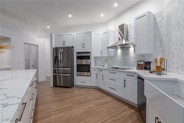 kitchen with wall chimney exhaust hood, tasteful backsplash, stainless steel appliances, light hardwood / wood-style floors, and white cabinets