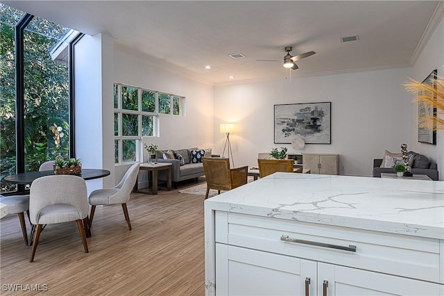 kitchen with crown molding, white cabinets, light stone counters, and light hardwood / wood-style floors