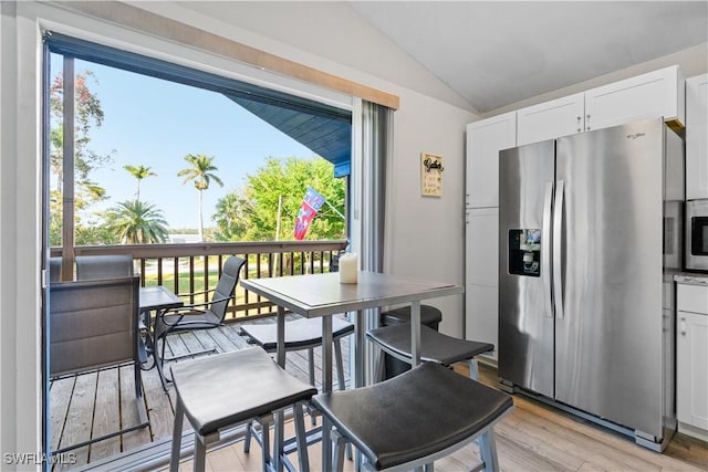 kitchen featuring vaulted ceiling, plenty of natural light, stainless steel fridge with ice dispenser, and white cabinets