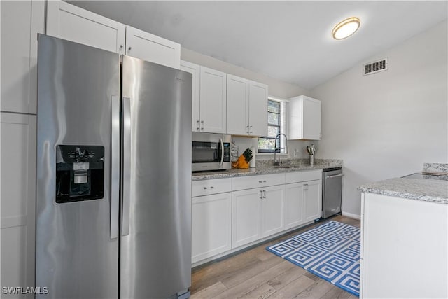 kitchen with sink, white cabinetry, vaulted ceiling, light wood-type flooring, and appliances with stainless steel finishes