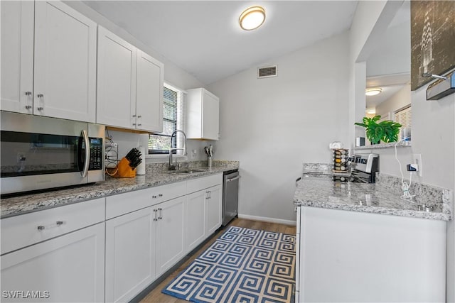 kitchen featuring sink, stainless steel appliances, light stone counters, white cabinets, and vaulted ceiling