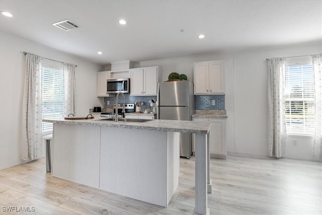 kitchen with stainless steel appliances, a kitchen island with sink, sink, and white cabinets