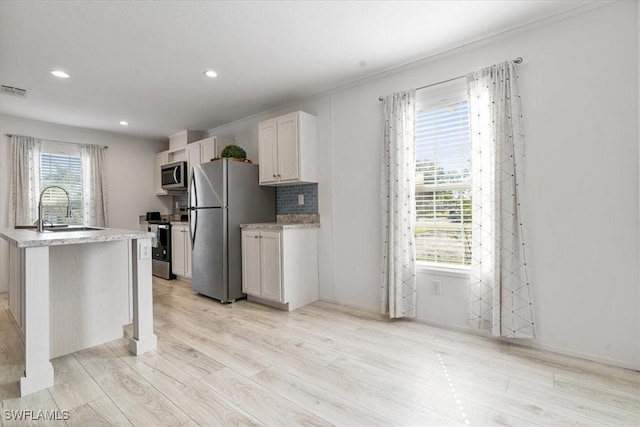 kitchen featuring sink, light hardwood / wood-style flooring, appliances with stainless steel finishes, white cabinets, and a center island with sink