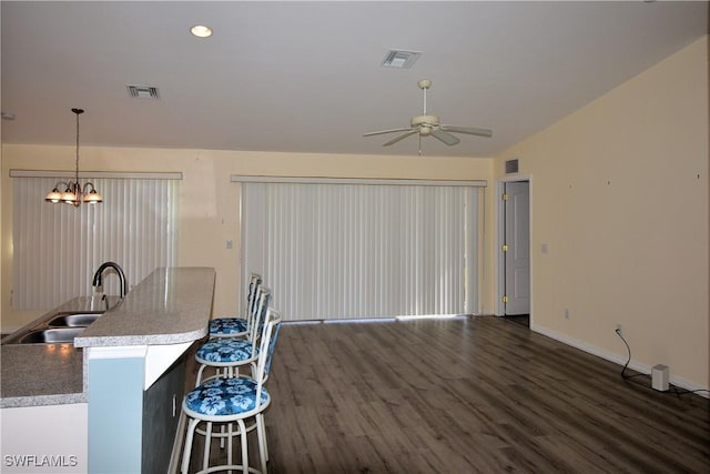 kitchen with pendant lighting, sink, dark wood-type flooring, a kitchen breakfast bar, and ceiling fan with notable chandelier