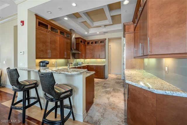 868 5th Ave S Unit 3A, Naples, FL 34102 - kitchen with a peninsula, light stone countertops, glass insert cabinets, wall chimney exhaust hood, and coffered ceiling