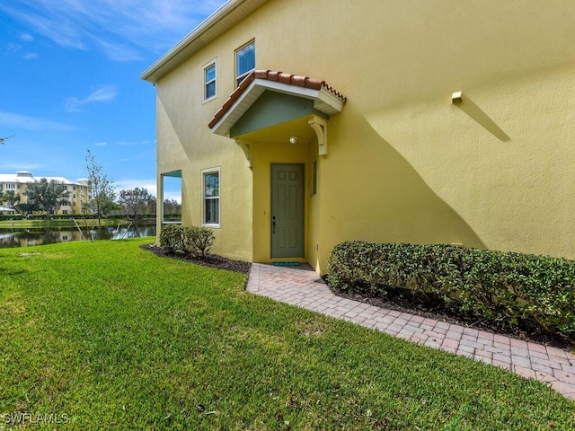 view of exterior entry featuring a water view and a yard