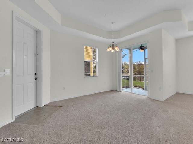 empty room featuring an inviting chandelier, light colored carpet, and a tray ceiling