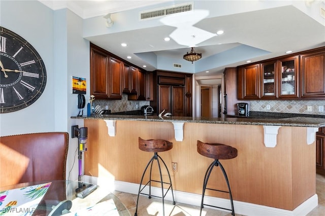 kitchen with a breakfast bar, kitchen peninsula, dark stone countertops, paneled built in fridge, and a tray ceiling