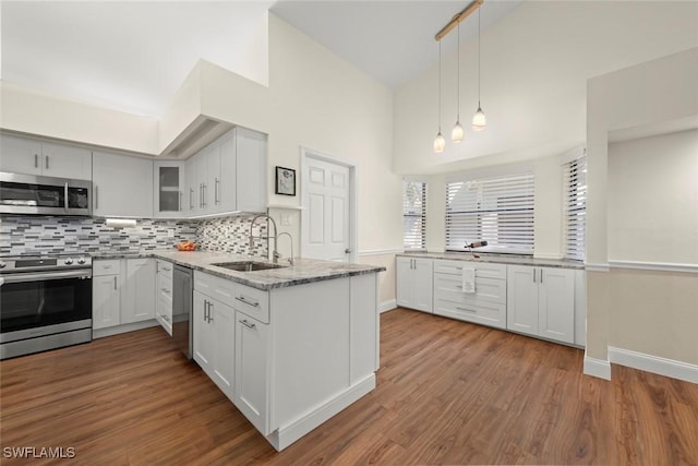 kitchen with appliances with stainless steel finishes, sink, white cabinets, hanging light fixtures, and hardwood / wood-style flooring