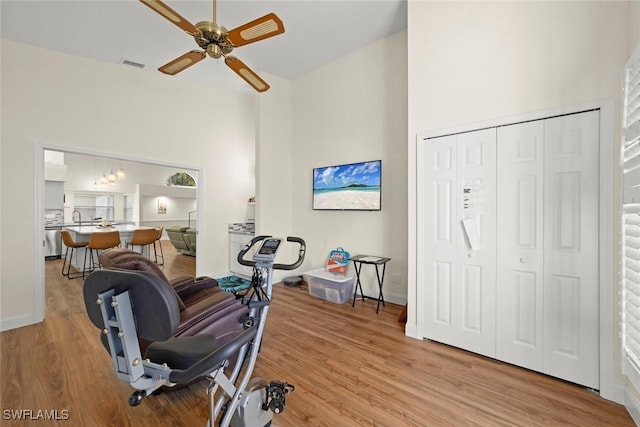 exercise area with sink, light hardwood / wood-style floors, ceiling fan, and a high ceiling