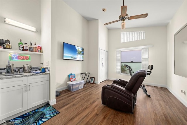 sitting room featuring ceiling fan, wood-type flooring, sink, and a towering ceiling