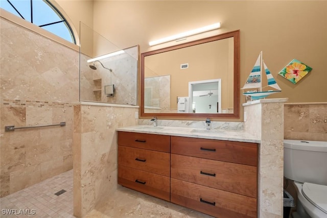 bathroom featuring vanity, toilet, tile walls, and a tile shower